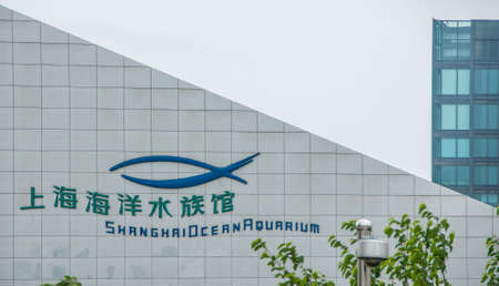 Shanghai, China - May 4, 2010: Pudong, Lujiazui district. Sign and logo in blue and green on white triangular wall of Shanghai Ocean Aquarium against silver sky. Green foliage.のeditorial素材