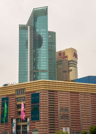 Shanghai, Pudong, Lujiazui, China - May 4, 2010: Green glass highrise buildings and Aurora Art Museum under silver sky. Colored flags in front.のeditorial素材