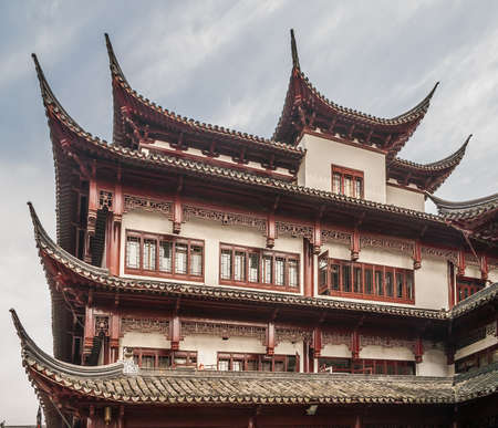Shanghai, China - May 4, 2010: Yuyuan shopping streets. Closeup of top corner of tall traditional Chinese architecture facade with white walls and red and brown woodwork for balconies, window frames and roof studs.のeditorial素材