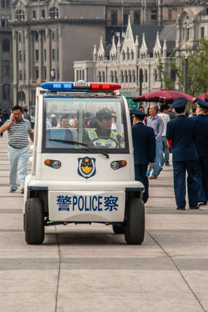 Shanghai, China - May 4, 2010: Closeup of white-blue police electrical vehicle with officer at wheel on boardwalk full of pedestrians along Huangpu River. Buildings as backdrop.のeditorial素材