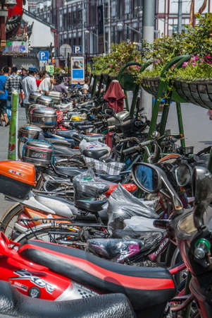 Shanghai, China - May 4, 2010: Closeup of row of parked motrobikes on side of road with green plant baskets above. People and buildings in back.のeditorial素材
