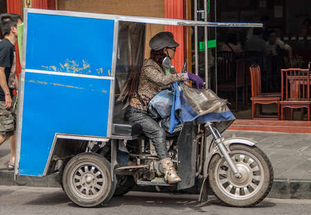Shanghai, China - May 4, 2010: Closeup of woman in leopard skin garb riding a motor tricycle with blue closed loading compartment. Street scene.のeditorial素材