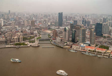 Shanghai, China - May 4, 2010: Aerial wider view on gray Wusong river emptying in brown Huangpu River at green park and Waibaidu bridge with highrise buildings. Smog on horizon.のeditorial素材