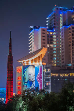 Shanghai, Xuhui, China - May 3, 2010: Night portrait. Colorfully lighted residential skyscraper peeps over dark trees of Xujiahui Park. Red slender tower is next with Swatch billboard.のeditorial素材