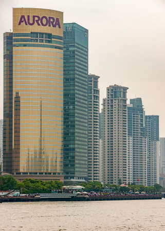 Shanghai, Pudong, Lujiazui, China - May 4, 2010: Closeup of golden Aurora skyscraper and others on side under silver sky behind boardwalk and Huangpu River.のeditorial素材
