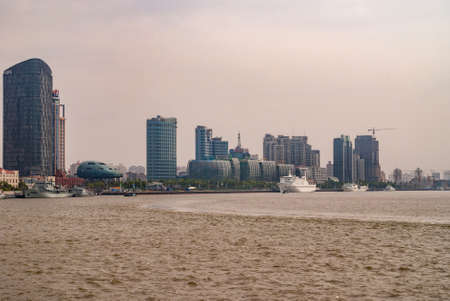 Shanghai, Pudong, Lujiazui, China - May 4, 2010: SIPG skyscraper and glass buildings along Huanpu river Cruise terminal with ship docked, under sliver-smog-brown sky.のeditorial素材