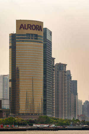 Shanghai, Pudong, Lujiazui, China - May 4, 2010: Closeup of golden Aurora skyscraper and others on side under silver- smog-brown sky behind boardwalk and Huangpu River.のeditorial素材