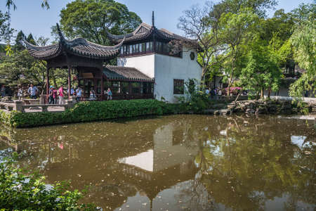 Suzhou China - May 3, 2010: Humble Administrators Garden. Brown-white structure in Chinese architecture set in pond surrounded by green foliage under blue sky. People present.のeditorial素材
