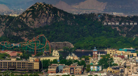 Suzhou China - May 3, 2010: Aerial overview shot of Amusement Land with roller coaster and other attraction and buildings. Back is partly green covered mountain and more of them on horizon.のeditorial素材
