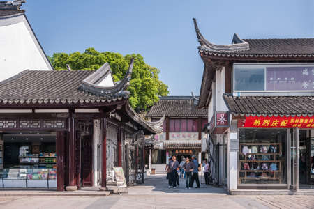Suzhou China - May 3, 2010: Shopping street with low white and gray traditional buildings as small shops. Pedestrians walking. Green foliage and blue sky.のeditorial素材