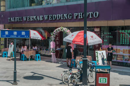 Suzhou China - May 3, 2010: Row of small shops waiting for customers, one being wedding photography with spot to shoot. People, bikes, umbrella and table with stairs.のeditorial素材