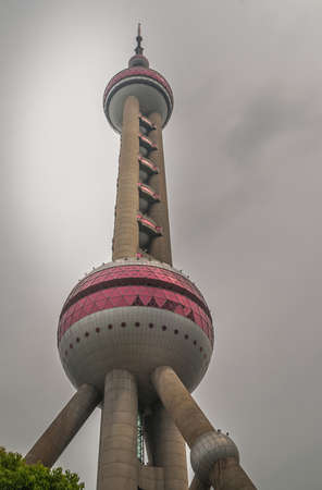 Shanghai, China - May 4, 2010: Closeup from bottom up on Oriental Pearl TV tower under dark rainy sky. Some green foliage.のeditorial素材