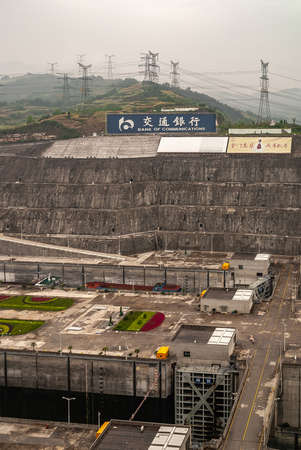 Three Gorges Dam, China - May 6, 2010: Yangtze River. Foggy morning, Billbords above adjacent ship lifts Beige concrete and hills with electrical pylons on horizon. Green garden in between.のeditorial素材