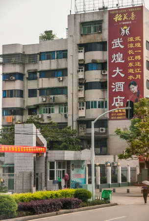 Chenjiawan, China - May 5, 2010: Tall gray residential building with large red-yellow billboard showing female and lots of Mandarin symbols. Street view with people.のeditorial素材
