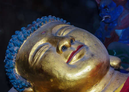 Fengdu, China - May 8, 2010: Ghost City, historic sanctuary. Closeup of smiling golden Buddha head of lying down statue with red lips and blue hair.のeditorial素材