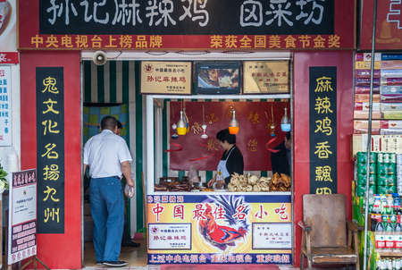 Fengdu, China - May 8, 2010: Closeup of red painted small take-out restaurant with lots of Mandarin symbols in white, and gold. Clients and vendor with display of prepared chicken meat.のeditorial素材