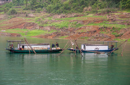 Wuchan, China - May 7, 2010: Dawu or Misty Gorge on Daning River. Closeup of Workets on cabn boats along fish pens in emerald green water with green covered mountain slope in back.のeditorial素材