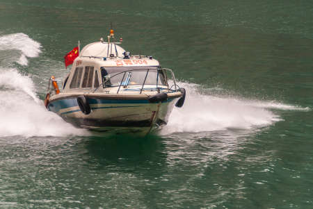 Wuchan, China - May 7, 2010: Dawu or Misty Gorge on Daning River. Closeup of  approaching white and blues law enforcement speed boat on emerald green water creating white surf.のeditorial素材
