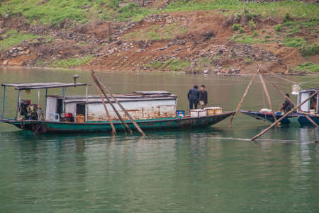 Wuchan, China - May 7, 2010: Dicui Gorge on Daning River. Closeup of workers talking on cabin boats upon emerald green water near fish pens with brown and green agriculture mountain slopes.のeditorial素材