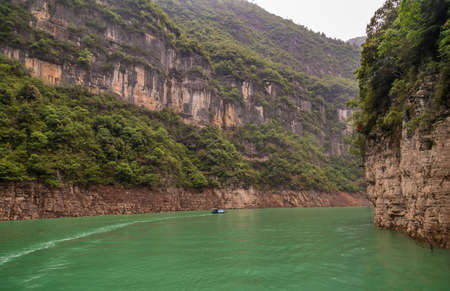 Wuchan, China - May 7, 2010: Dawu or Misty Gorge on Daning River. Bend in canyon with brown rocky cliffs, green foliage on top and small boat on emerald green water.の写真素材