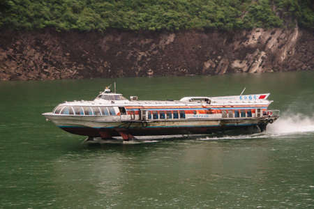 Baidicheng, China - May 7, 2010: Qutang Gorge on Yangtze River. Meteor fast, rocket-like, rusty white passenger ferry on green water with brown rocky shoreline and some green vegetation on top.のeditorial素材