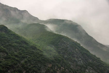 Baidicheng, China - May 7, 2010: Qutang Gorge on Yangtze River. Landscape of gray cloudscape descends in waves along slopes of green covered mountain.の写真素材
