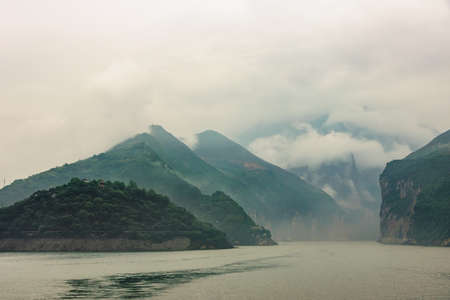 Baidicheng, China - May 7, 2010: Qutang Gorge on Yangtze River. Landscape of wide view into canyon with misty cloudscape descending off green mountain slopes. Green water up front.の写真素材