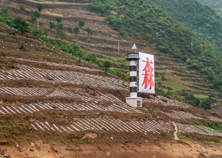 Baidicheng, China - May 7, 2010: Qutang Gorge on Yangtze River. Brown agricultural plots on green mountain slope with red navigation sign and light signal pole.の写真素材