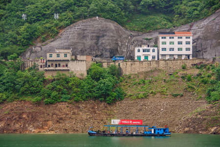 Guizhou, China - May 6, 2010: Xiling gorge on Yangtze River. blue floating gas station fo boats on green water with red Sinopec banner. Multi-level housing on green mountain slope of the town.のeditorial素材