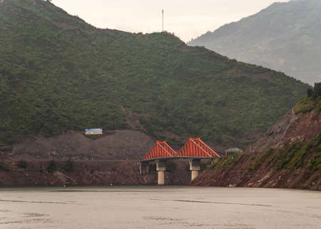Shengli Street, China - May 6, 2010: Xiling gorge on Yangtze River.Closeup of  Red bridge links X210 and X239 roads above green water with green foliage covered mountains.の写真素材
