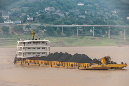 Fengdu, Chongqing, China - May 8, 2010: Yangtze River. Closeup of yellow barge with heaps of black...