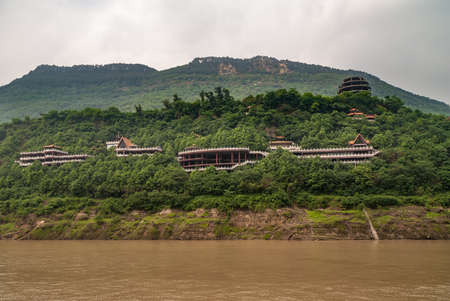 Fengdu, Chongqing, China - May 8, 2010: Yangtze River. Classic architecture style red roofs popping above green forest on hill slope at large monstery. Some silver cloudscape.の写真素材