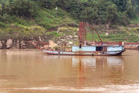 Huangqikou, Chongqing, China - May 8, 2010: Yangtze River. inactive light blue dredging vessels moored along forested green shoreline on brown water.の写真素材