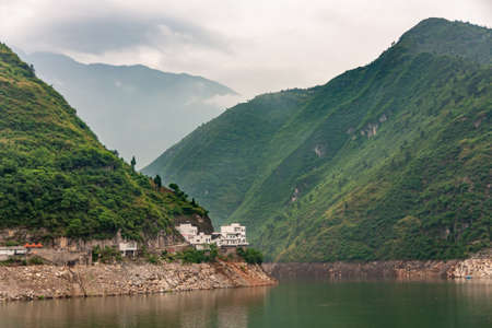 Guandukou, Hubei, China - May 7, 2010: Wu Gorge in Yangtze River. White buildings built on edge of green water in bend in canyon of green mountains and cloudscape.の写真素材