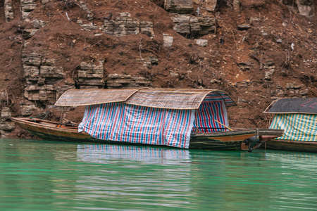 Wushan, Chongqing, China - May 7, 2010: Mini Three Gorges. Closeup of covered tourist sampans docked against brown cliff rock behind emerald green water. Cover add color.のeditorial素材