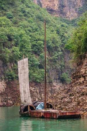 Wushan, Chongqing, China - May 7, 2010: Mini Three Gorges. Round cabins on sloops with sail docked with pontoon against brown cliffs with higher up green vegetation and on emerald green water.のeditorial素材