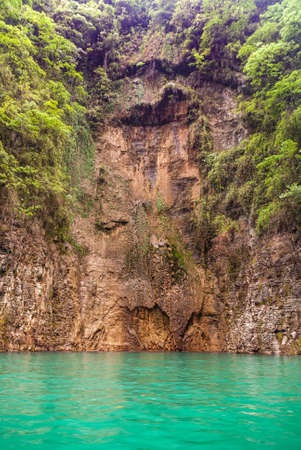 Wushan, Chongqing, China - May 7, 2010: Mini Three Gorges on Daning River. Water drips out of slid in brown cliff rocks above emerald green water. Green foliage on sides.のeditorial素材