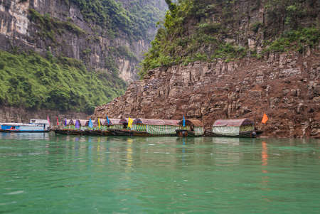 Wushan, Chongqing, China - May 7, 2010: Mini Three Gorges. ten covered tourist sampans with docked against brown cliff rock  behind emerald green water. Green foliage. Flags add color.のeditorial素材