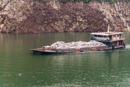 Guandukou, Hubei, China - May 7, 2010: Wu Gorge in Yangtze River. Barge transporting white bags sails on green water in front of brown rock shoreline.のeditorial素材