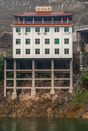 Wushan, Chongqing, China - May 7, 2010: Wu Gorge in Yangtze River. Closeup of white Hotel-Restaurant with red Chinse style roof, built on stilts at entrance of Daning River.のeditorial素材
