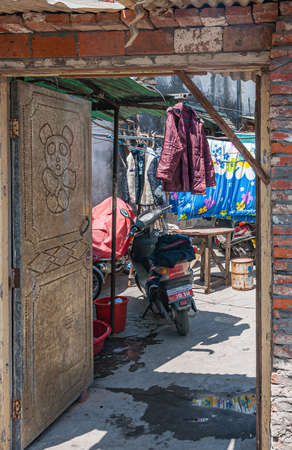 Tongli, JIangsu, China - May 3, 2010: Hutong network of narrow walkways, simple housing, and small businesses. Open heavy door with panda image to courtyard of house in alley. laundery adds color.のeditorial素材