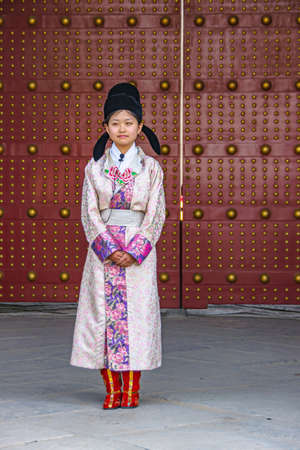 Xian, China - April 30, 2010: Closeup of young woman in traditional rose and blue garb, red boots and black cap, in front of giant red door in North Gate of Shuncheng City Wall.のeditorial素材