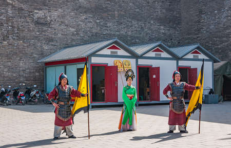Xian, China - April 30, 2010: Welcome ceremony show in front of North Gate of Shuncheng City Wall. 2 guards with yellow flags and young woman in traditional green dress and large head piece.のeditorial素材