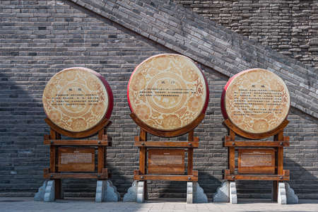 Xian, China - April 30, 2010: Welcome ceremony show in front of North Gate of Shuncheng City Wall. Closeup of 3 beige and Chinese traditional drumson brown wooden stand against gray stone wall.のeditorial素材