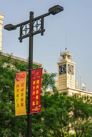 Xian, China - April 30, 2010: Downtown view. White clock tower and yellow and red banners against blue sky with green foliage.のeditorial素材
