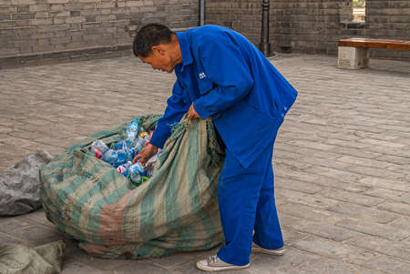 Xian, China - April 30, 2010: Downtown view. One male worker in blue garb sorts recyclable plastics on gray stone surface with bags on his sides.のeditorial素材