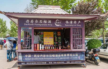 Xian, China - May 1, 2010: Purple booth on wheels of Danruoer Pomegranate Brewery on parking square with bottles on dispaly and servants ready. Green foliage around.のeditorial素材
