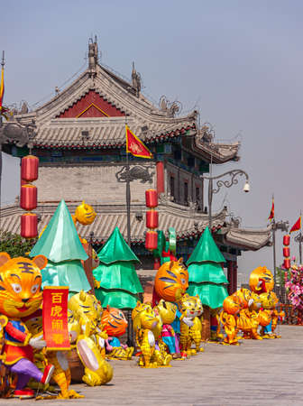 Xian, China - April 30, 2010: North Gate of Huancheng City Wall. Year of the Tiger display. Line of yellow tiger dolls, large and small, among fake green trees and red lanterns.のeditorial素材