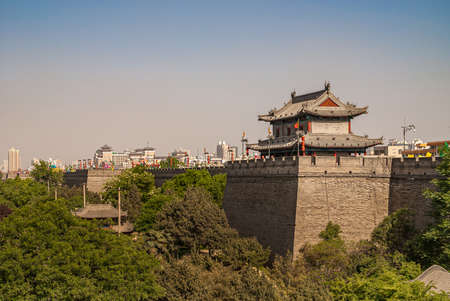 Xian, China - April 30, 2010: North Gate of Huancheng City Wall. Wide shot of small gray tower building in traditional Chinese architecture just east of gate under blue smog sky. Red ornaments and green foliage.のeditorial素材