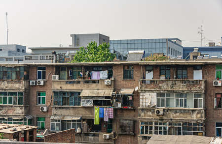 Xian, China - May 1, 2010: Old residential brown brick housing with dilapidated balconies, AC systems and laundry hanging to dry under silver sky.のeditorial素材
